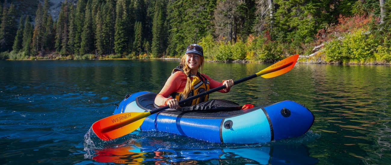 A smiling woman in a packraft paddles in the water