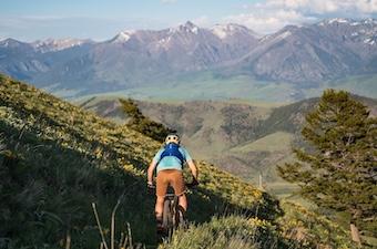 A man riding away from us on a trail with large mountains in the background